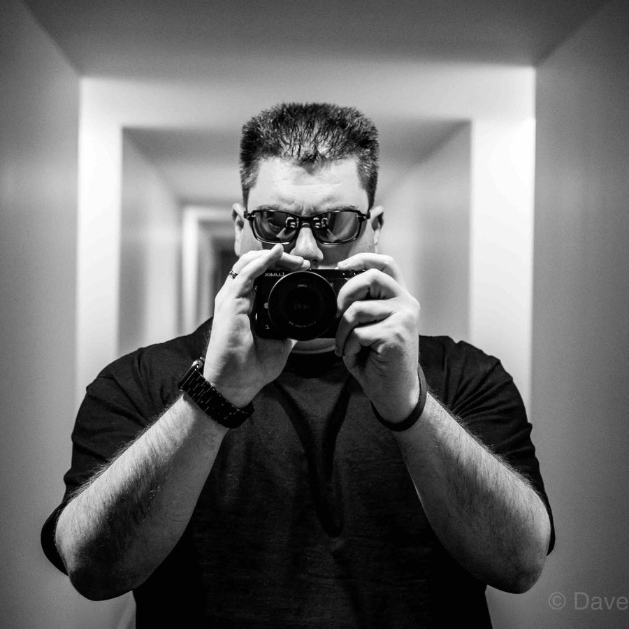 Dave Howard, black-and-white self-portrait holding a camera